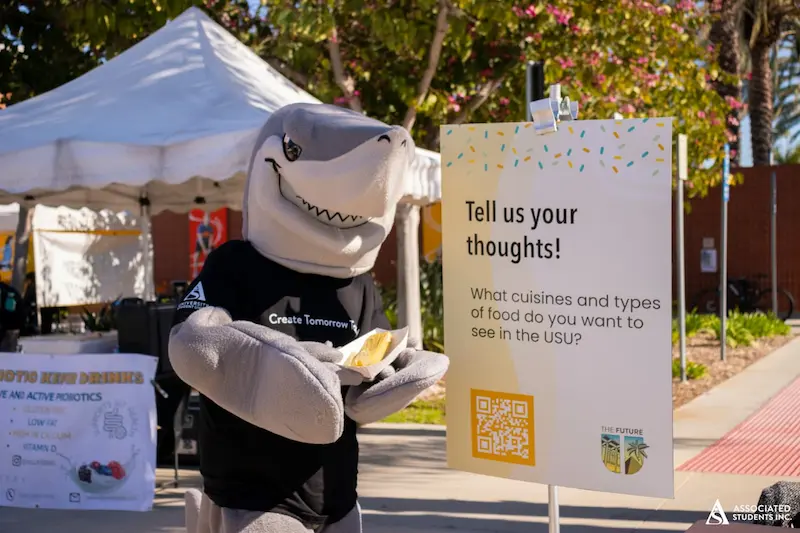 Elbee with poster asking "Tell Us Your Thoughts"